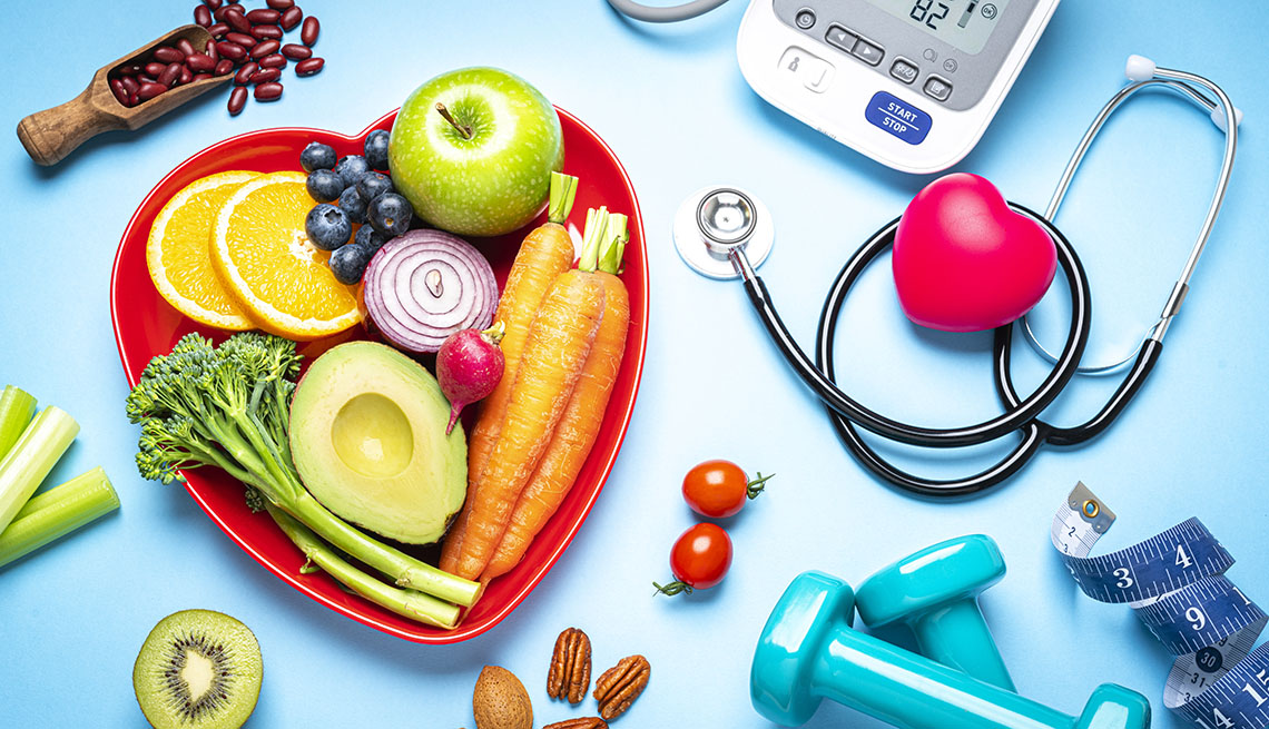 Healthy lifestyle concepts: red heart shape plate with fresh organic fruits and vegetables shot on blue background. A digital blood pressure monitor, doctor stethoscope, dumbbells and tape measure are beside the plate  This type of foods are rich in antioxidants and flavonoids that prevents heart diseases, lower cholesterol and help to keep a well balanced diet. High resolution 42Mp studio digital capture taken with SONY A7rII and Zeiss Batis 40mm F2.0 CF lens